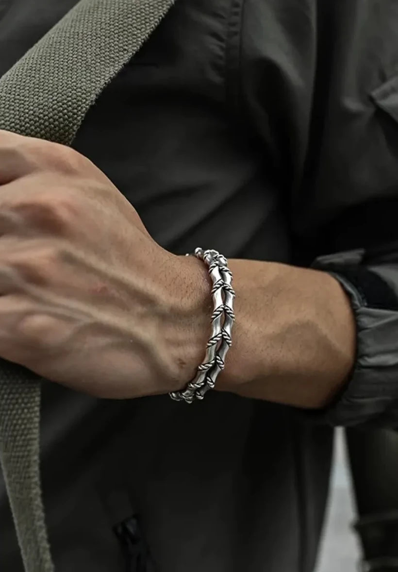 Close-up of the bangle on the wrist as the model grips a canvas strap, emphasizing the detailed texture of the silver against skin