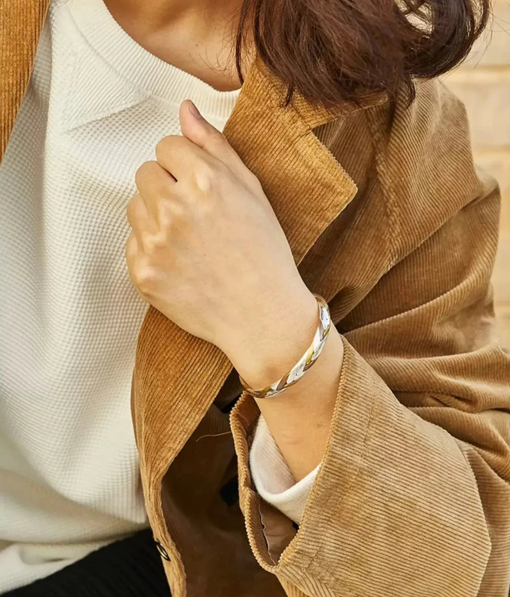Lifestyle shot of a hand resting against a brown corduroy jacket, wearing the twisted tricolor bangle for a vintage-inspired look