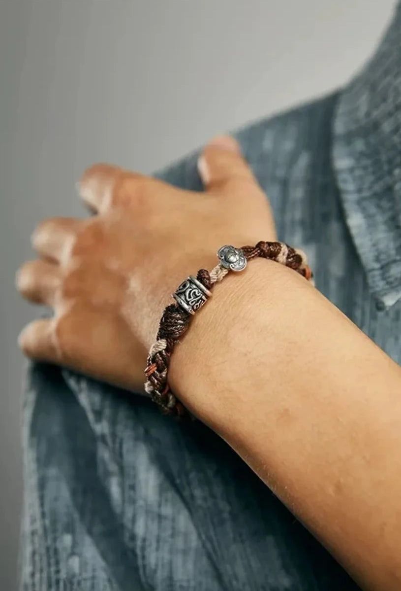 Close-up on the wrist showing the vintage finish of the silver charms against a textured denim shirt
