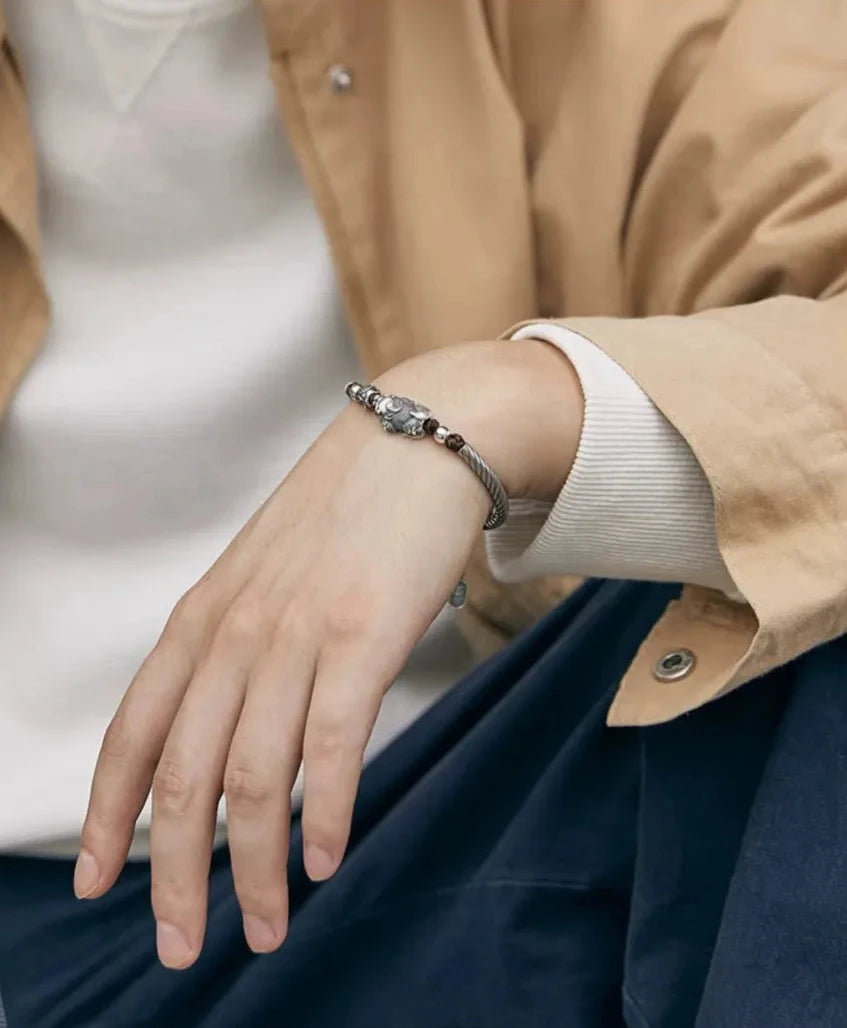 A relaxed pose showing the bracelet on the wrist, highlighting the contrast between the silver sheen and the coat fabric