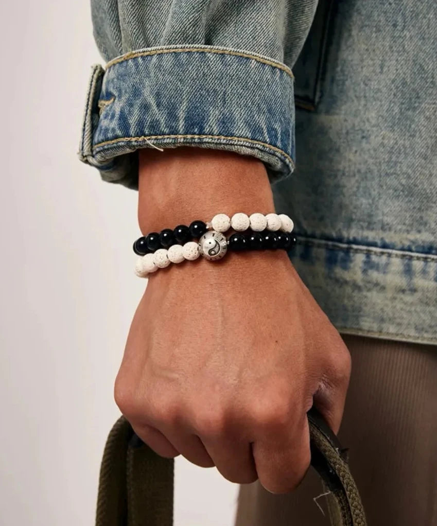 Lifestyle shot of a man holding a bag, wearing the stacked black and white bracelets with a denim jacket