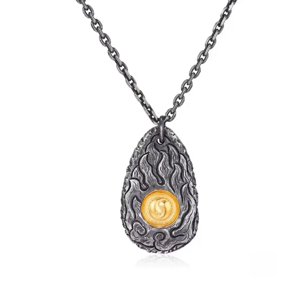 Front view of the teardrop-shaped pendant featuring a gold Yin Yang symbol surrounded by oxidized silver flame reliefs
