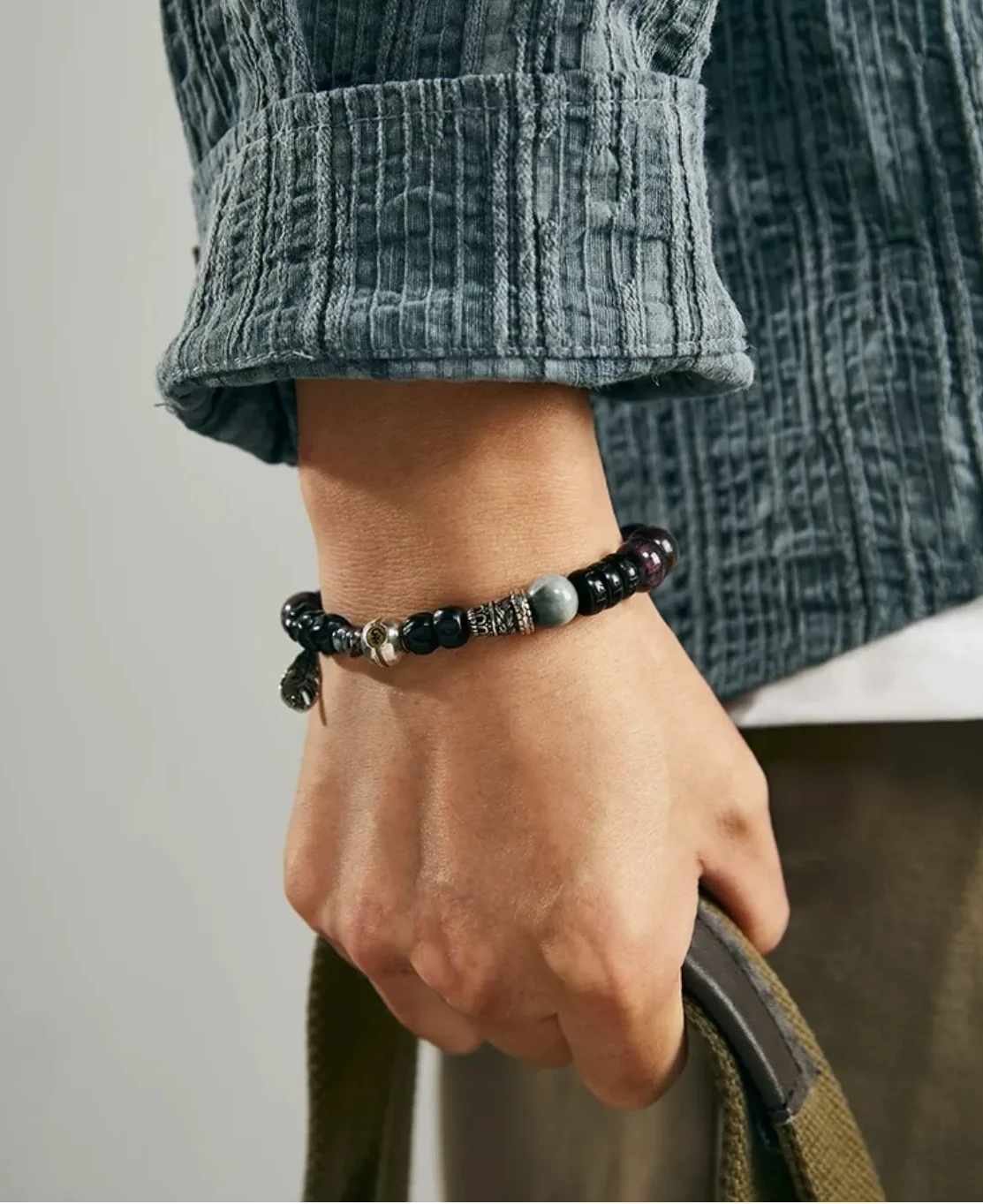 Lifestyle shot of a man holding a bag, wearing the bracelet which adds a touch of Zen boho style to a casual outfit